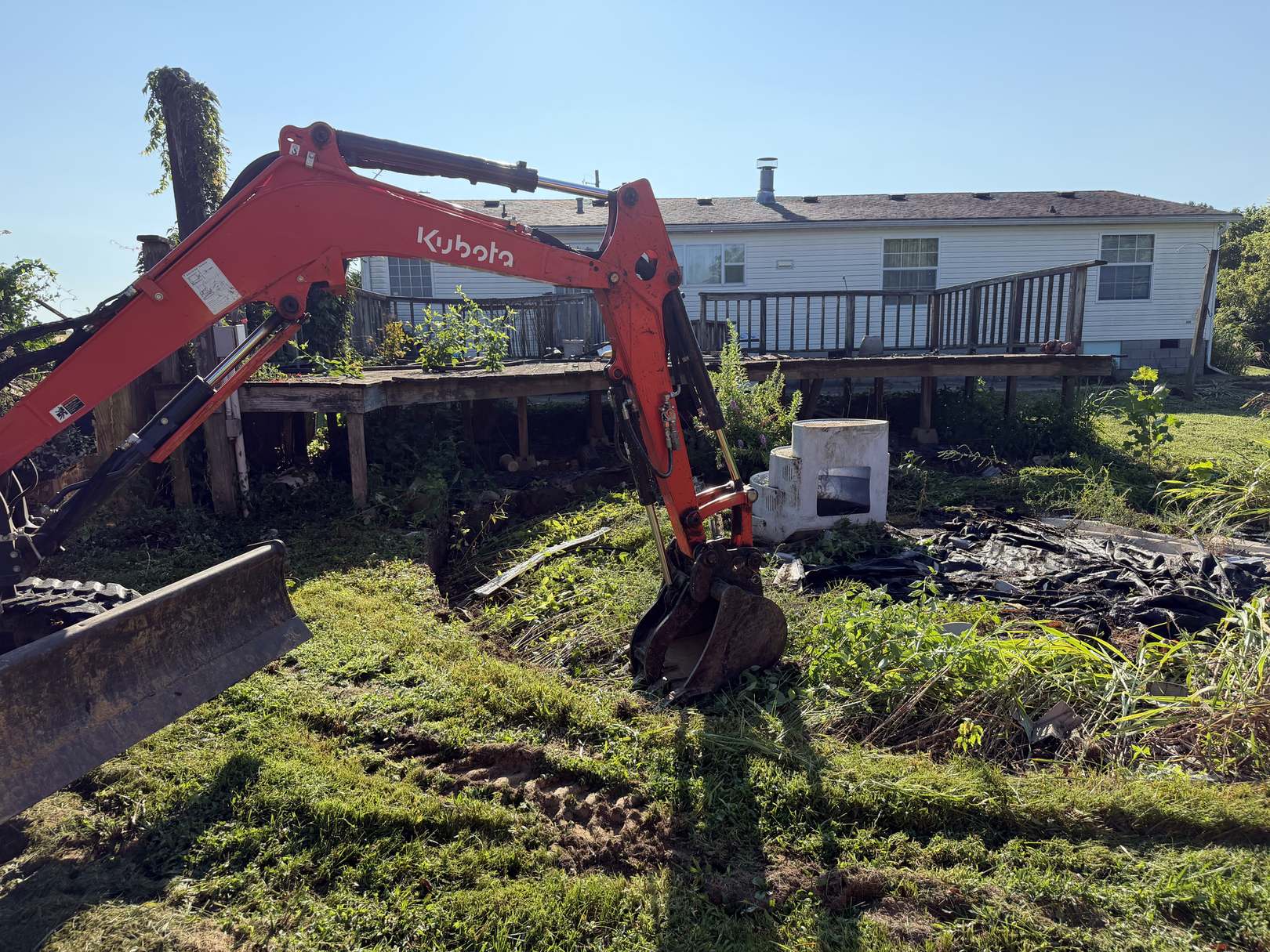 A mini excavator taking down a raised wooden deck behind a house