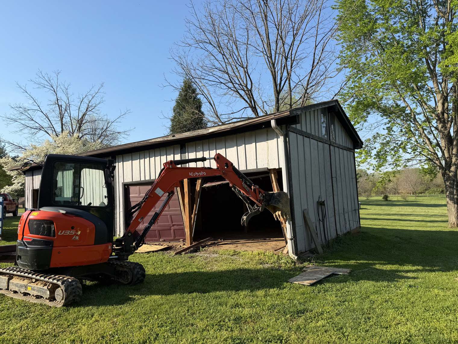A mini excavator starting to pull down the front of an old metal-sided garage