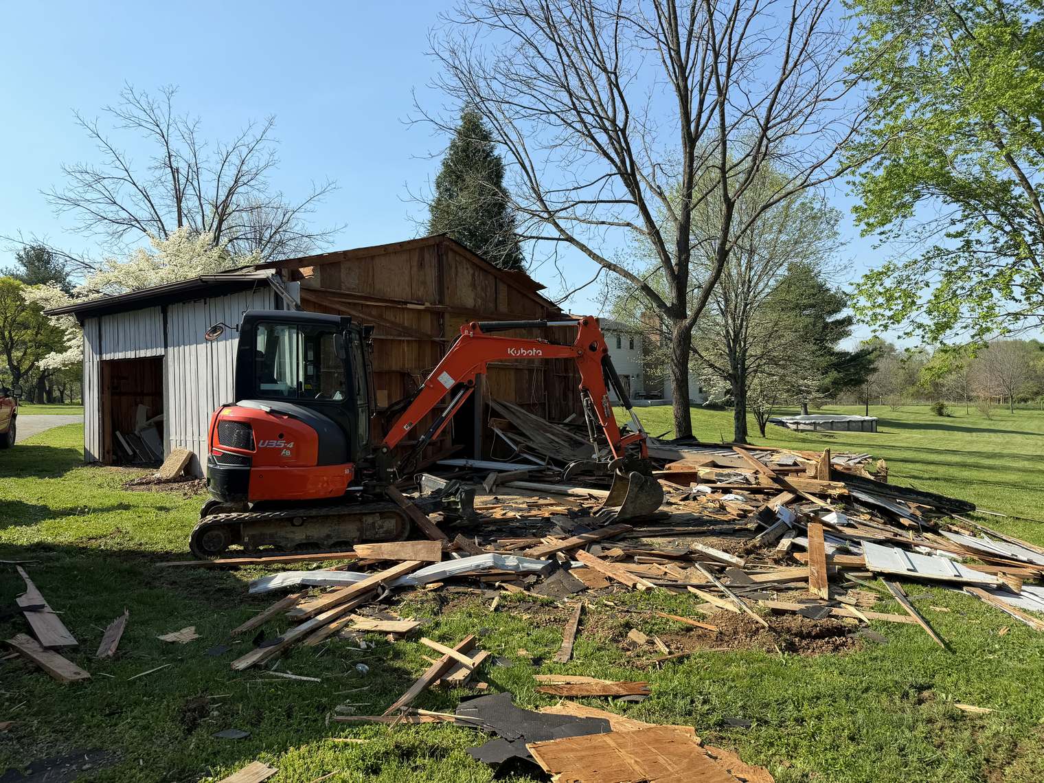 A Micro Man mini excavator pulling down an old wooden garage, debris spread across the lawn