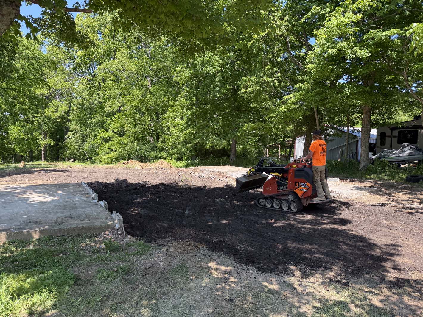 A cleared building pad after a teardown, a worker on a stand-on loader leveling the dirt