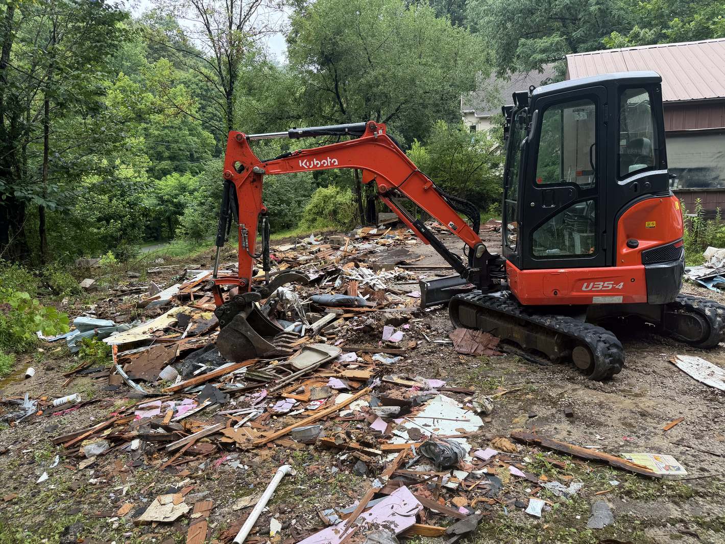 A mini excavator sorting teardown debris on a wooded lot